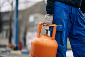 Propane Company Woodford County IL 1 Man carrying LPG gas bottle at gas station, representing Best Propane Prices Near Me and a Propane Company Woodford County IL trusts
